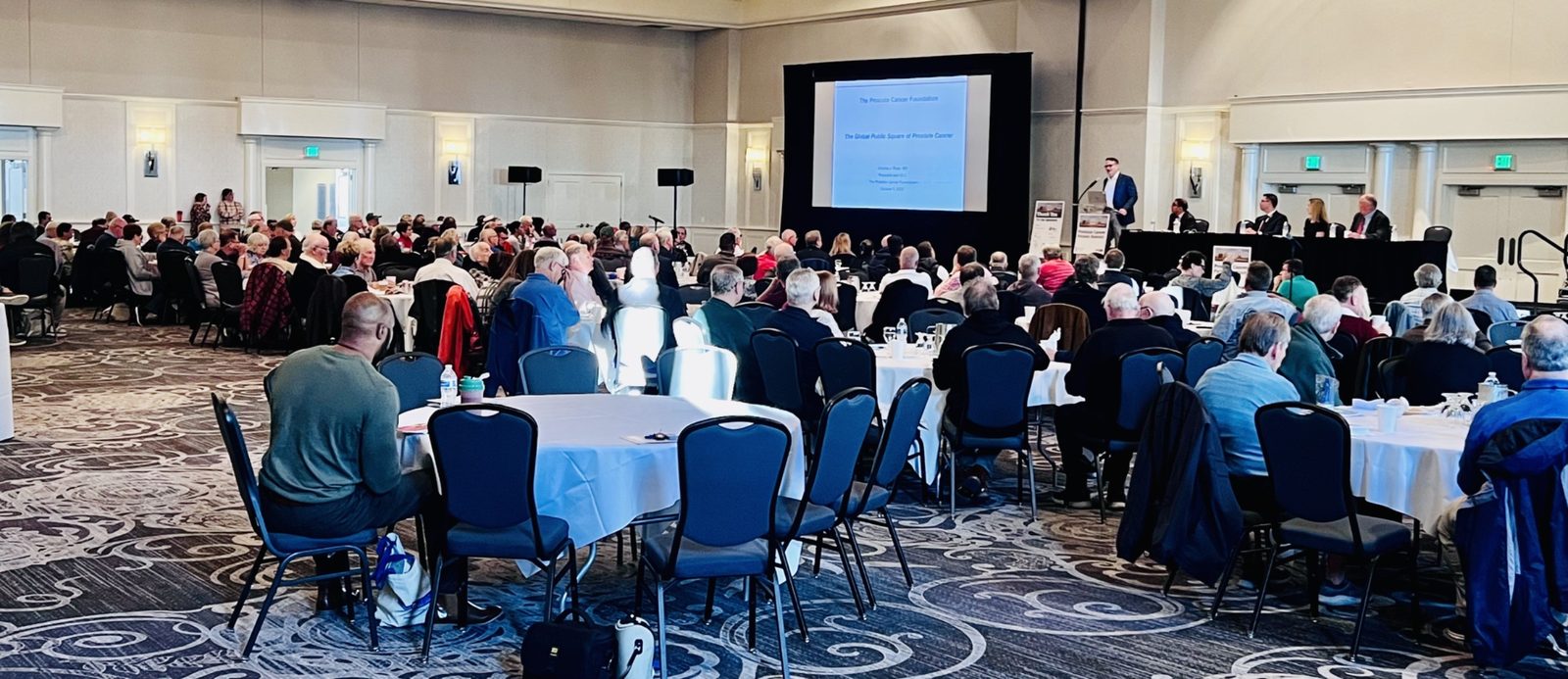 Attendees seated at the Milwaukee Prostate Cancer Patient Summit as a speaker presents from the stage